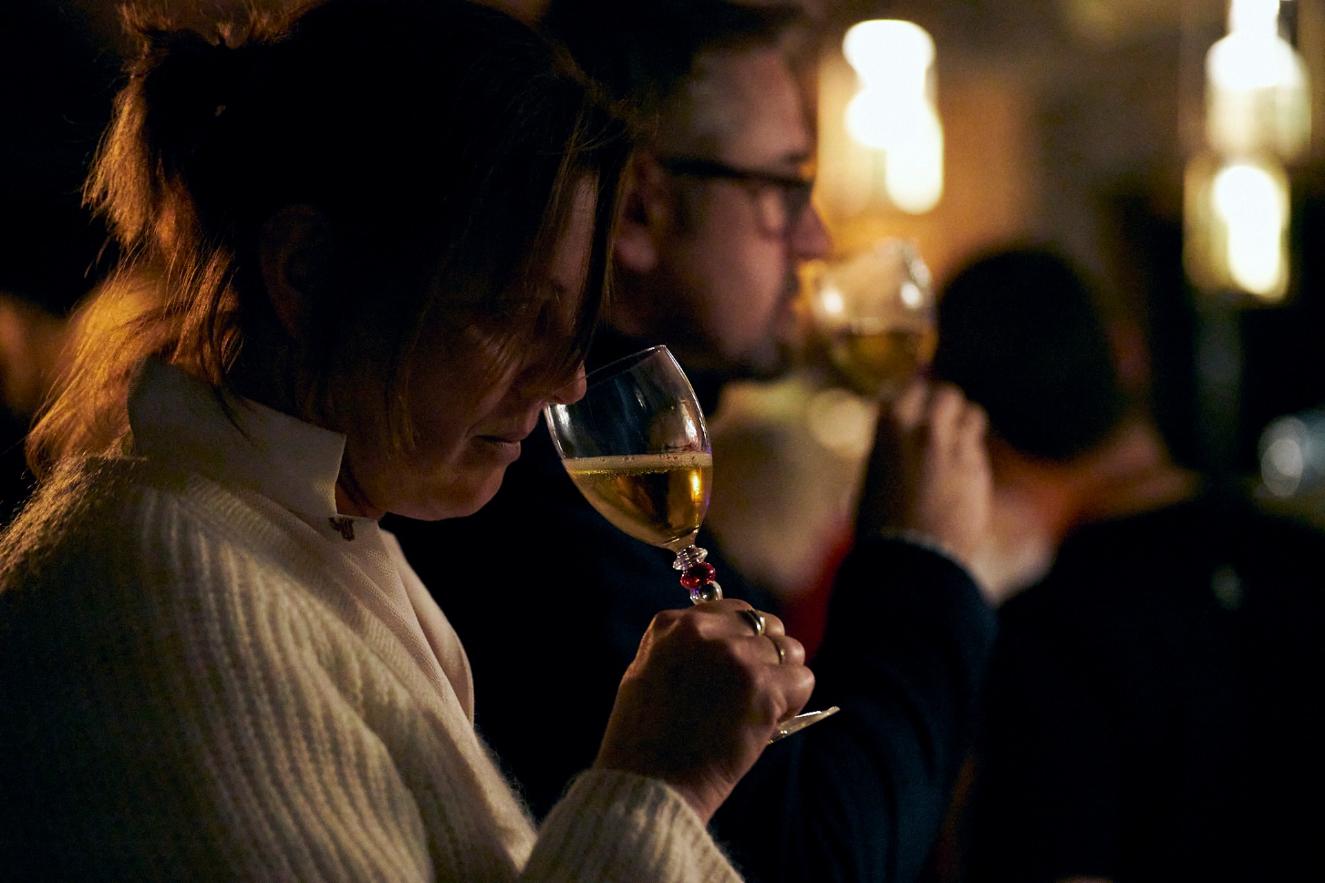Guest holding a wine glass in a warm, candlelit gathering.